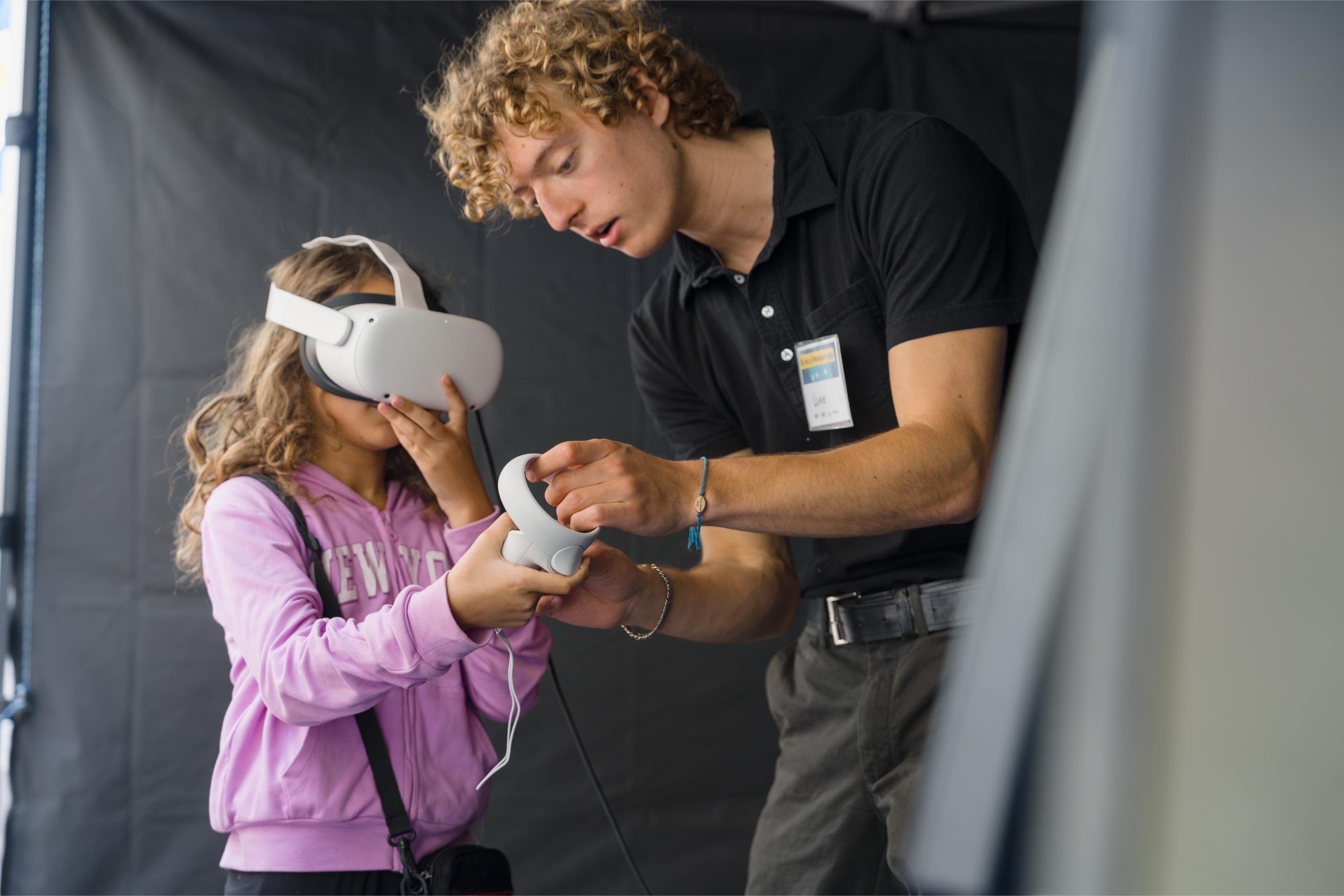 A volunteer shows the young participant how to use the controller at the Virtual Reality Games Booth.